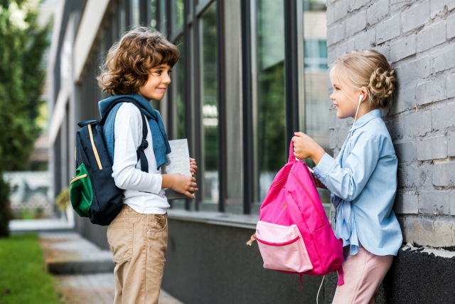 Iskolás kislány és iskolás kisfiú beszélgetnek az iskola előtt