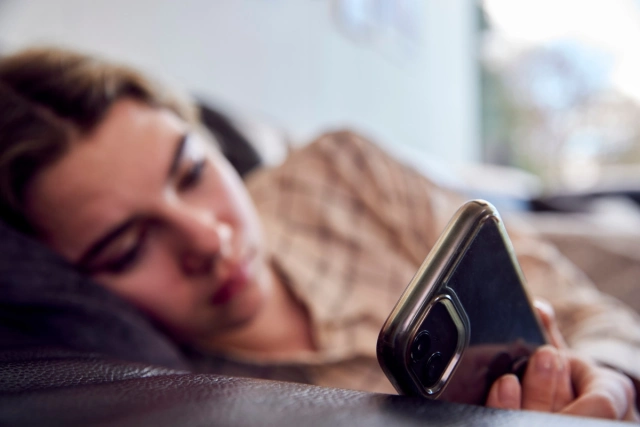 Kamasz lány fekszik az ágyon, és a telefonján lóg