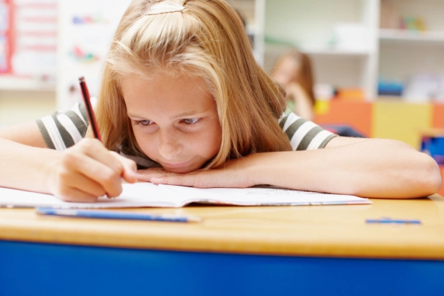 Első ostályos kislány a füzetébe ír.