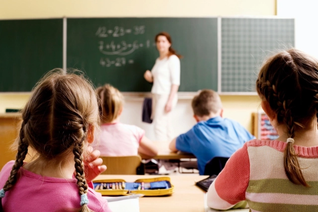 Tanár a táblánál áll, gyerekek figyelik az órát
