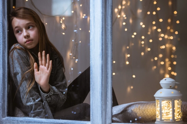 Kislány szomorúan néz ki az ablakon karácsonykor