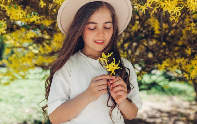kalapos kislány sárga aranyeső bokor előtt tavasszal